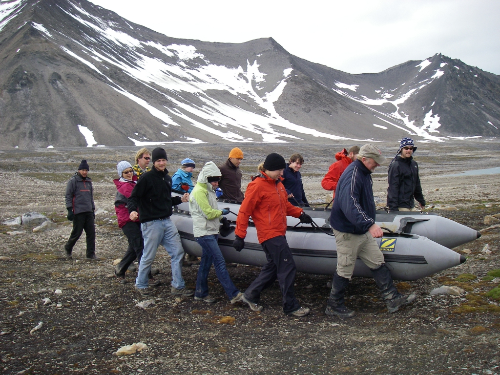 A group of people carries a boat down to a lake.