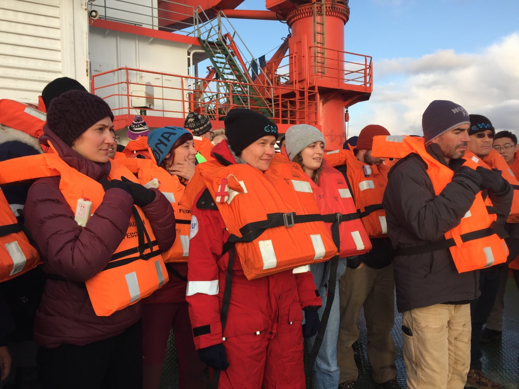 A group of people grouped on the deck of a ship ready for a safety drill. 